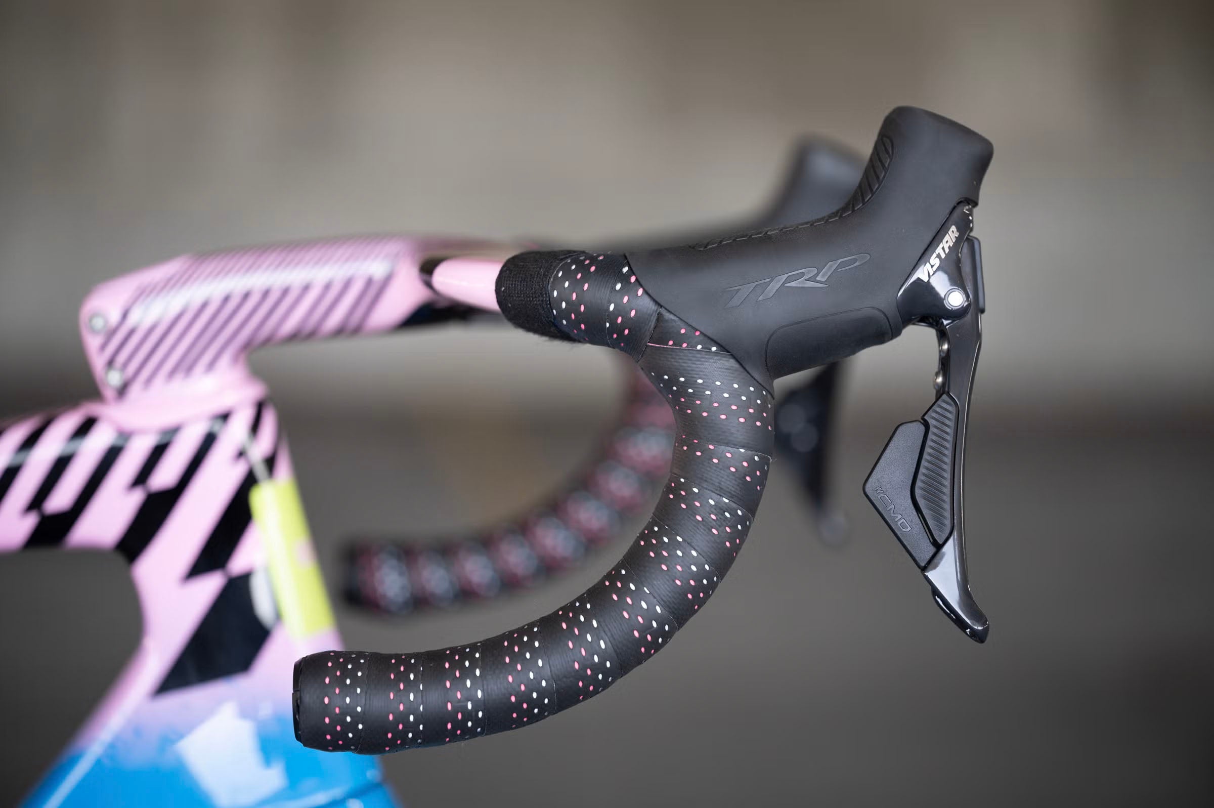 Close-up of a bicycle handlebar with TRP VISTAR levers, speckled grip and pink frame in the background