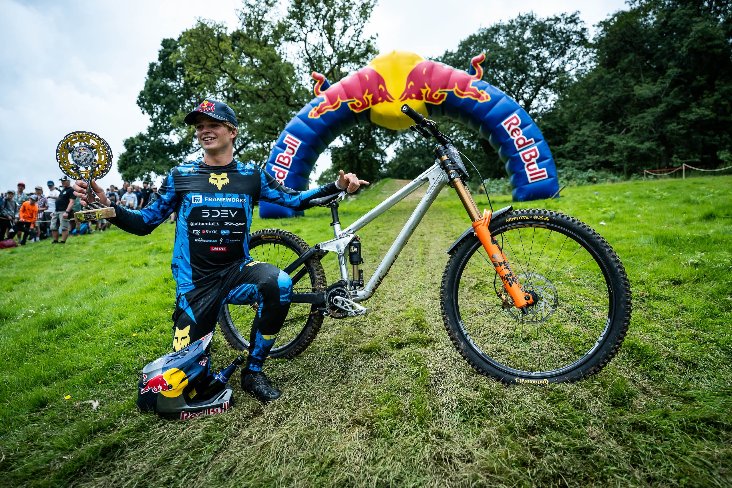 Biker in racing gear with a bike holding trophy on a grassy field