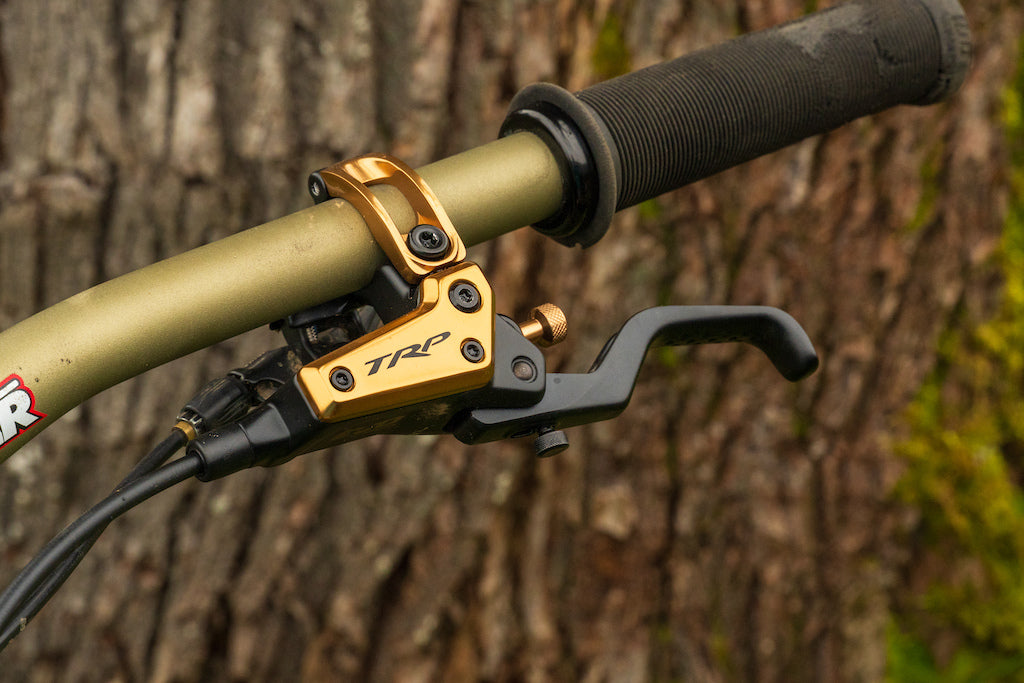 Close-up of a bike handlebar with gold TRP lever against a tree background