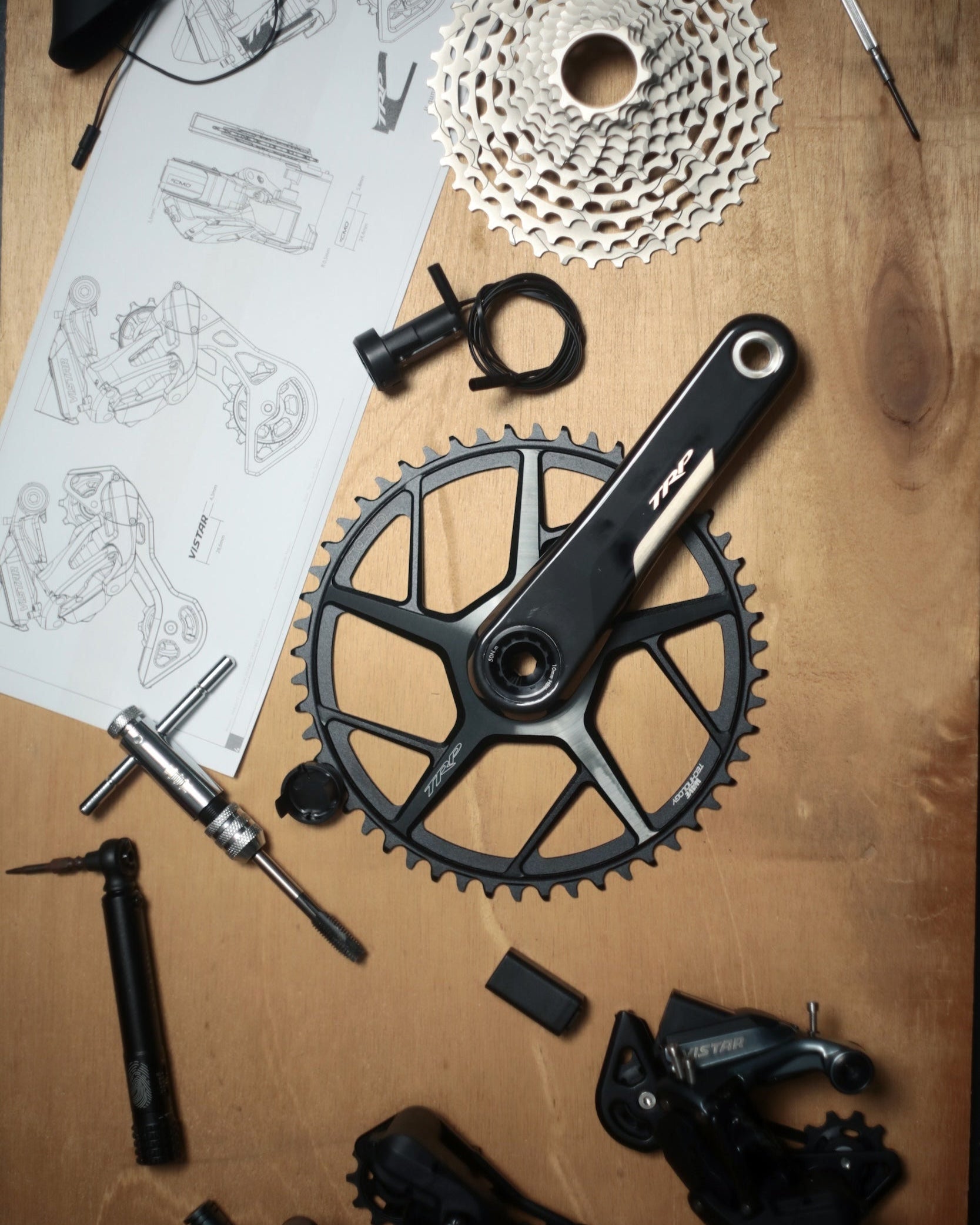 TRP Bicycle gear components and tools on a wooden surface with blueprints.