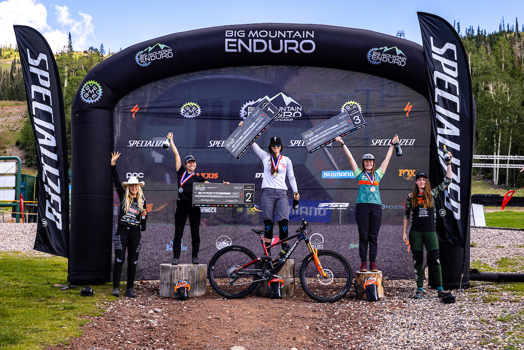 female bikers on a podium holding checks with a mountain bike in the foreground