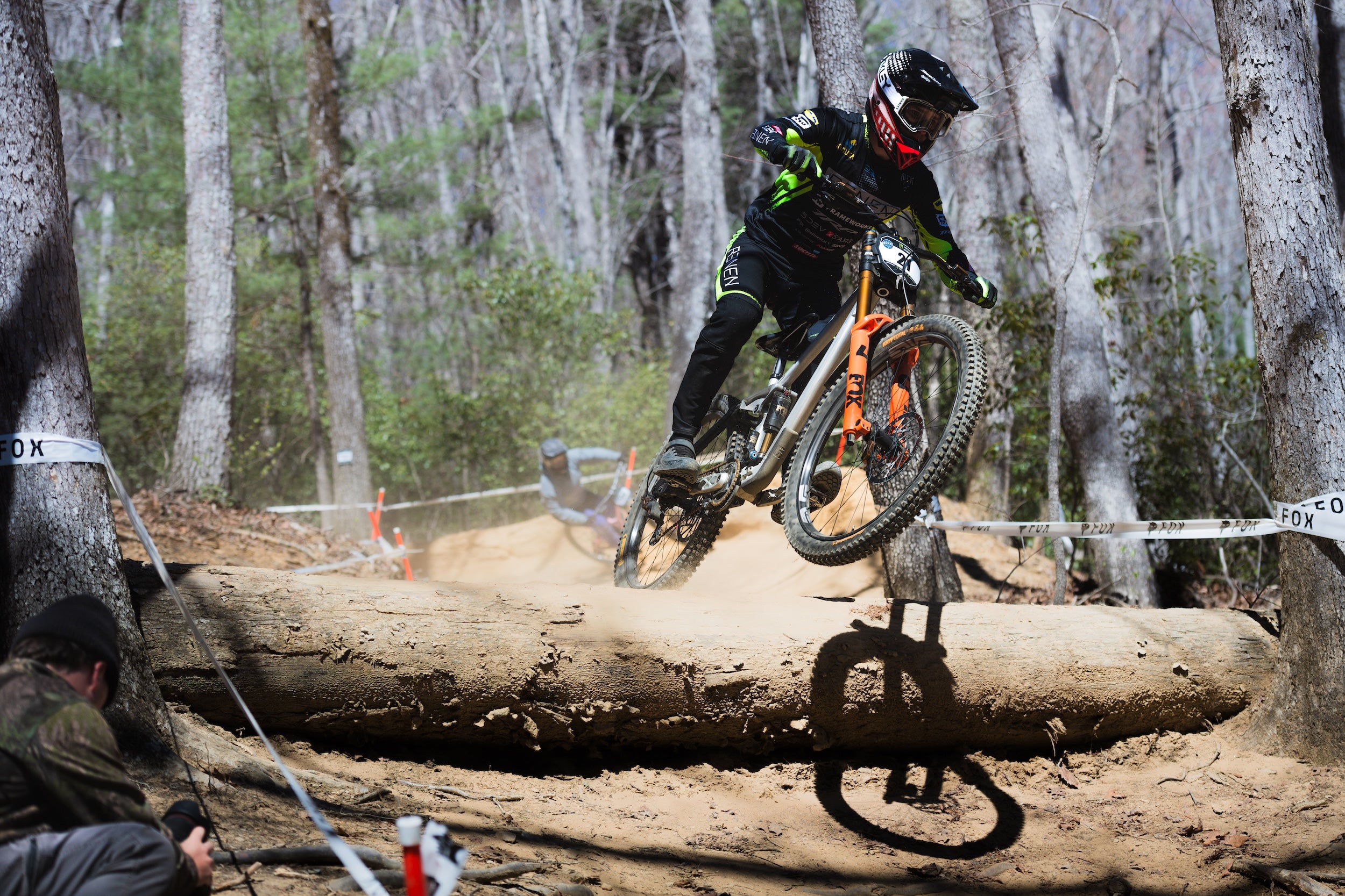Person riding a mountain bike over a log in a forest setting